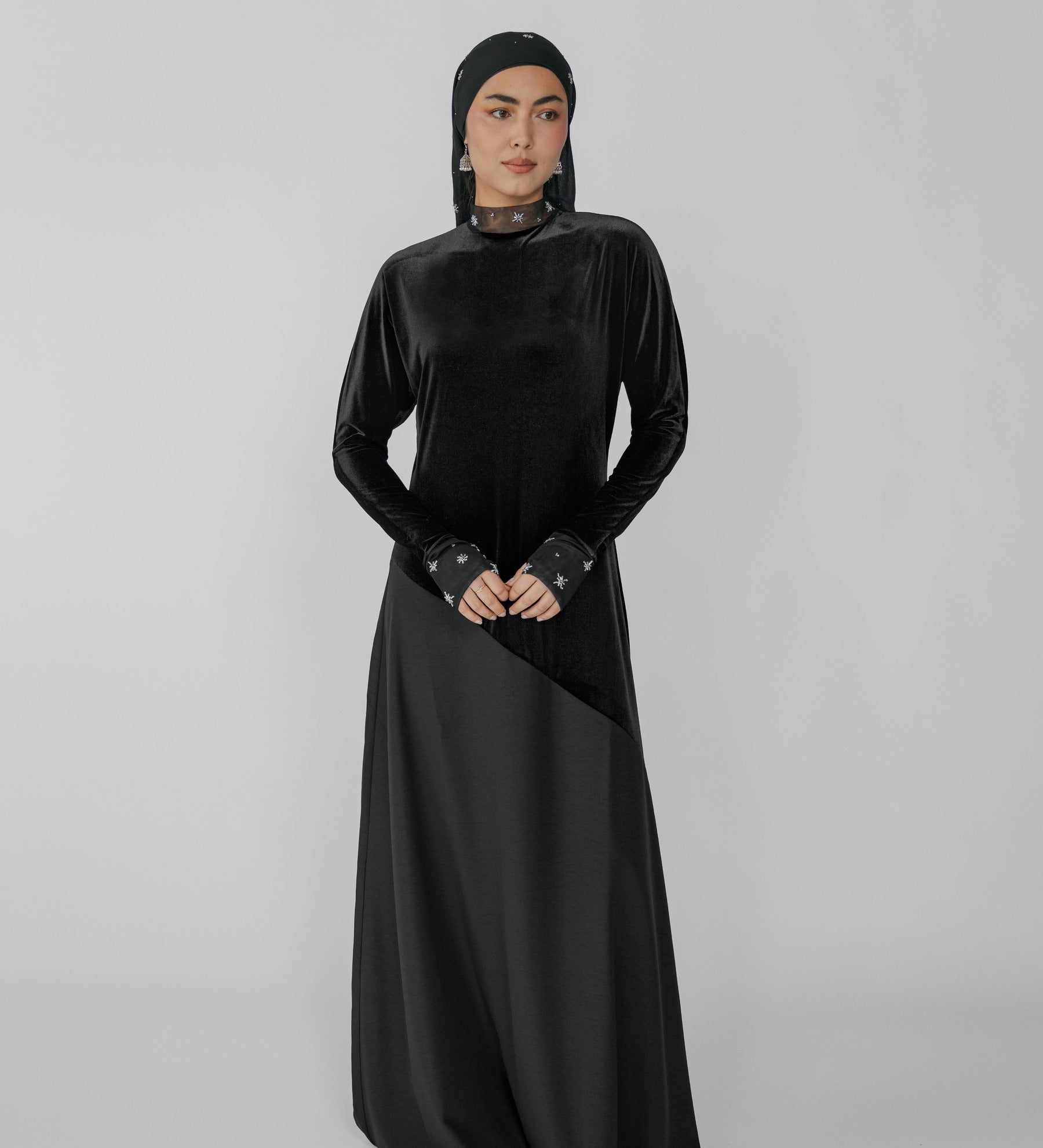 Woman wearing a black dress with a hijab on a gray background
