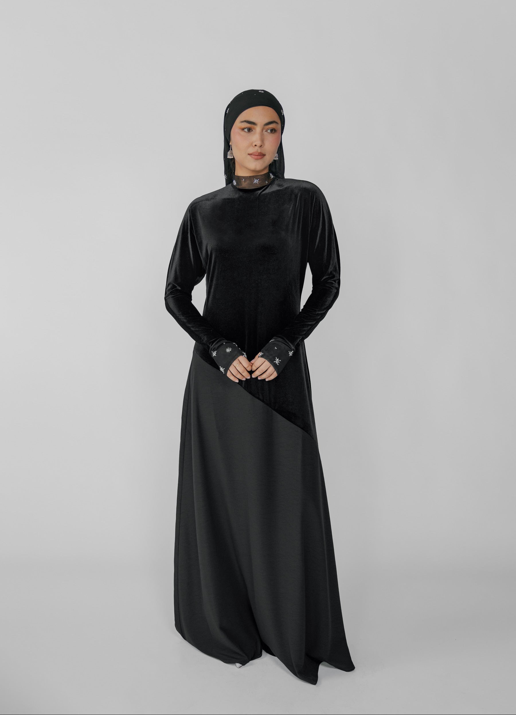 Woman wearing a black dress with a hijab on a gray background