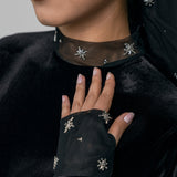 Close-up of a person wearing a black outfit with decorative elements, including earrings and a necklace.
