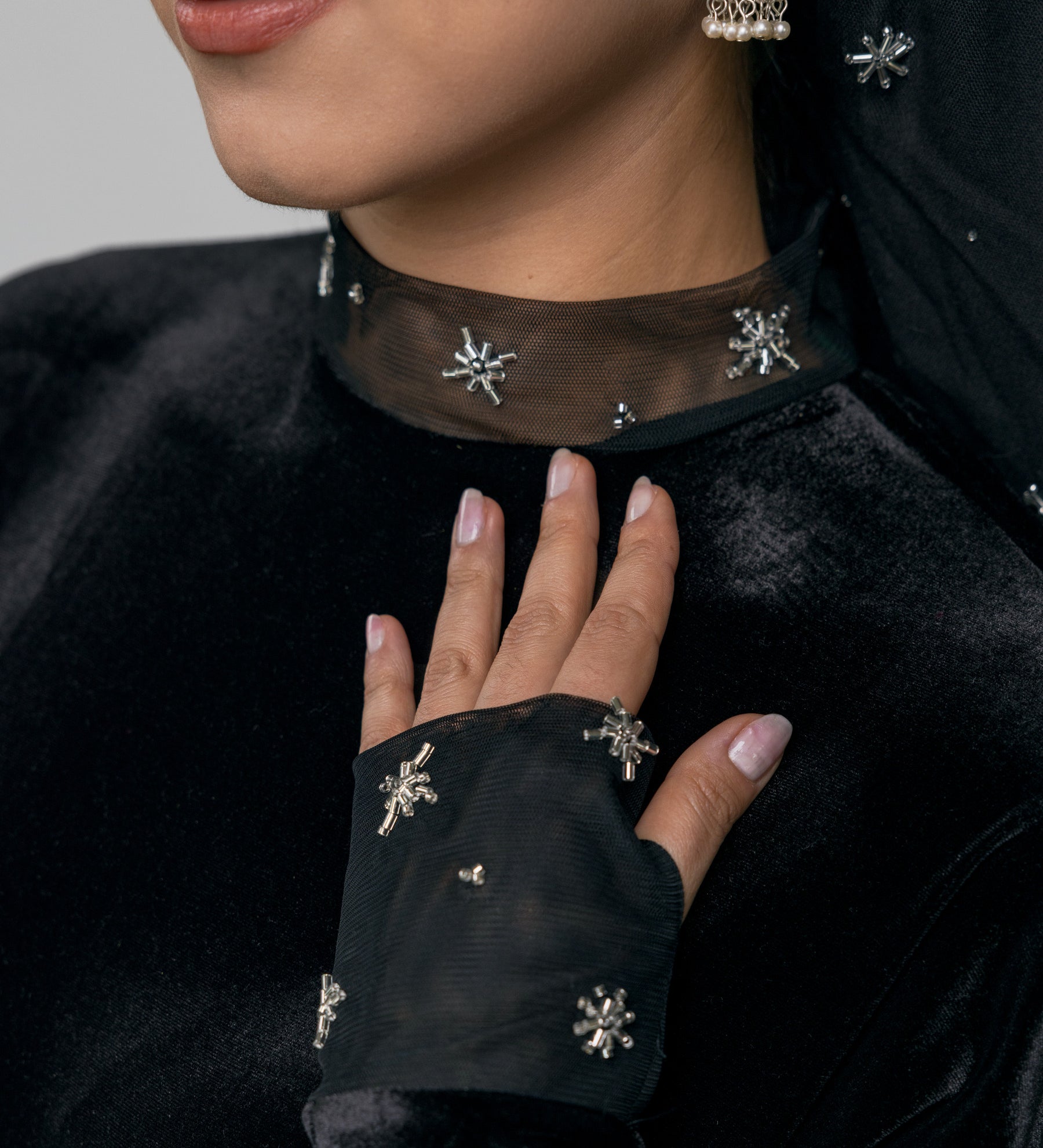 Close-up of a person wearing a black outfit with decorative elements, including earrings and a necklace.