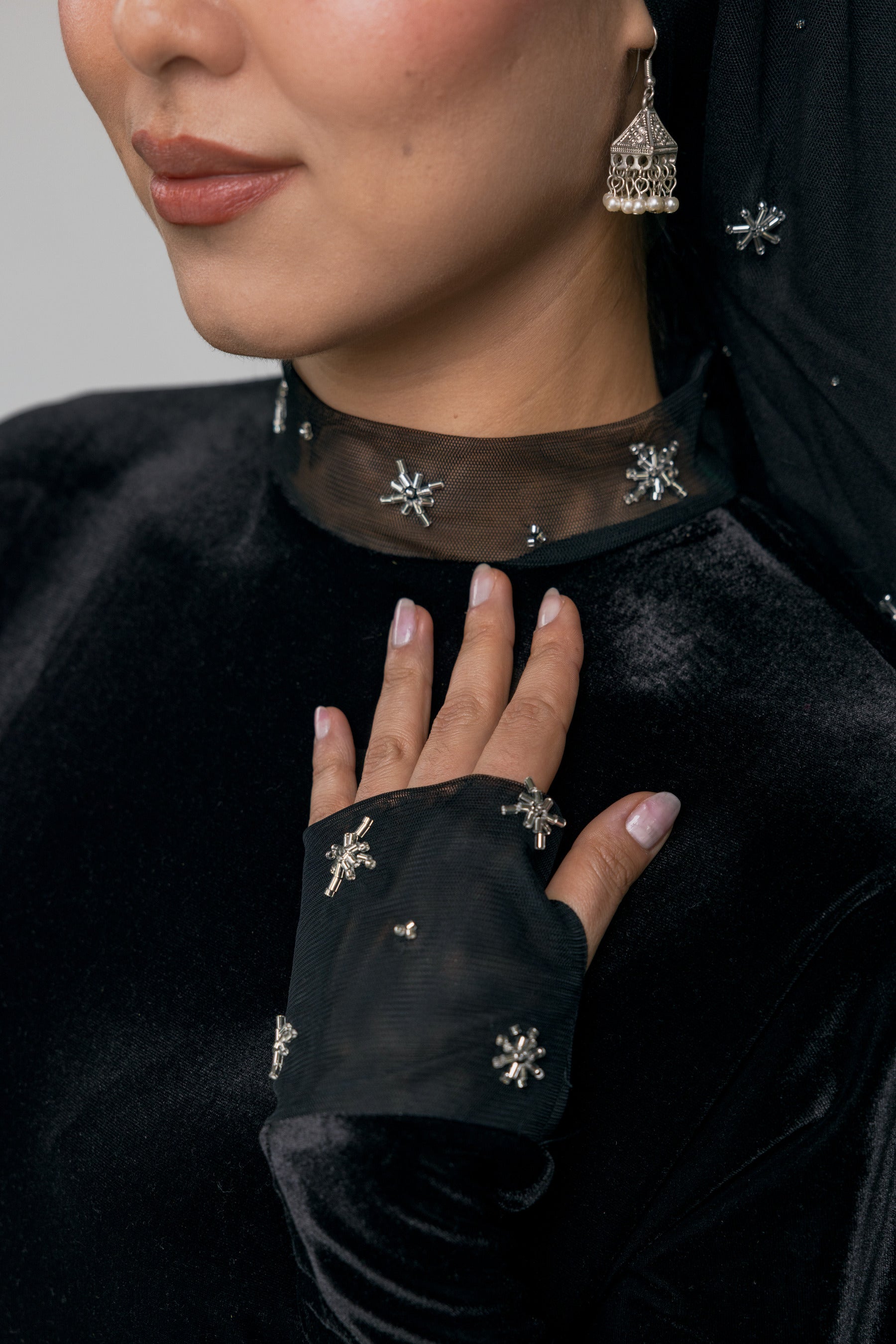 Close-up of a person wearing a black outfit with decorative elements, including earrings and a necklace.