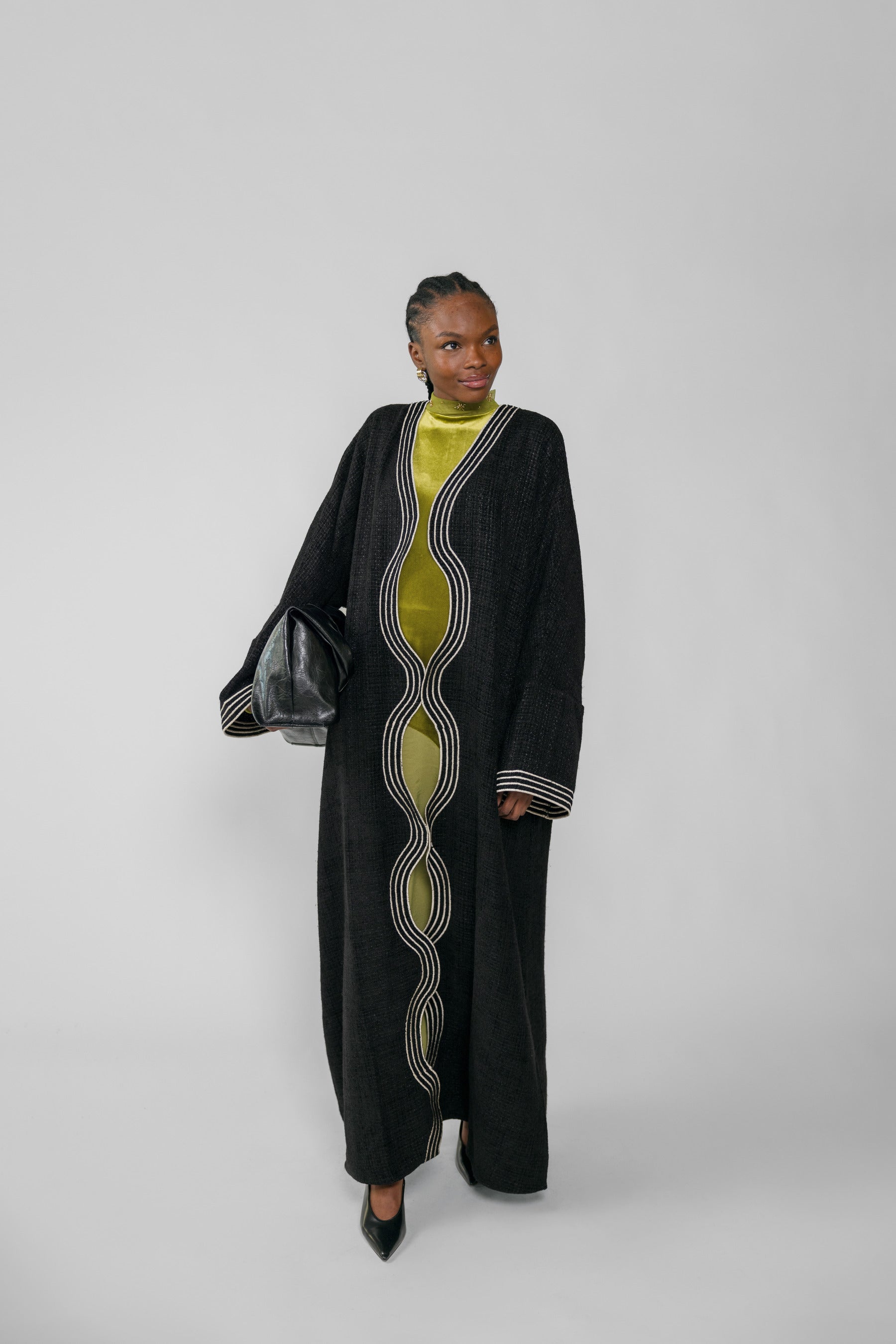 Woman wearing a long black abaya with green dress on a white background