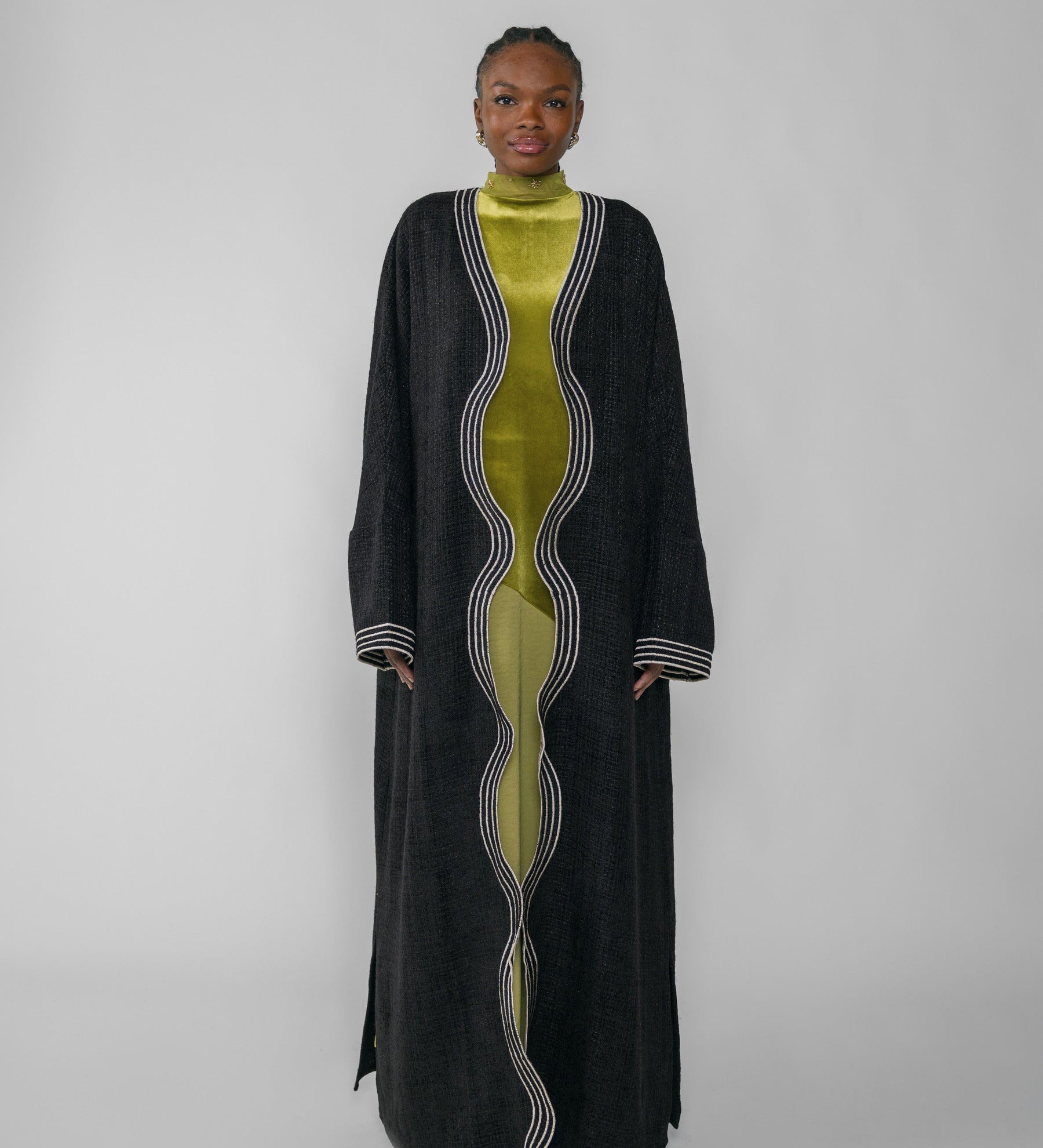 Woman wearing a black abaya and green dress with a white background