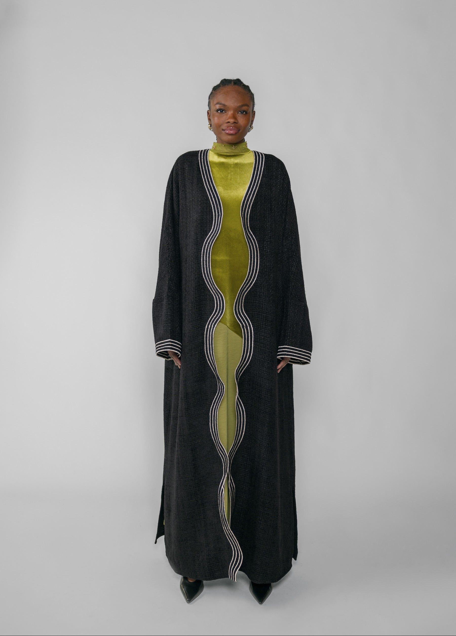 Woman wearing a black abaya and green dress with a white background