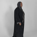 Person wearing a long black abaya with a hijab on a white background