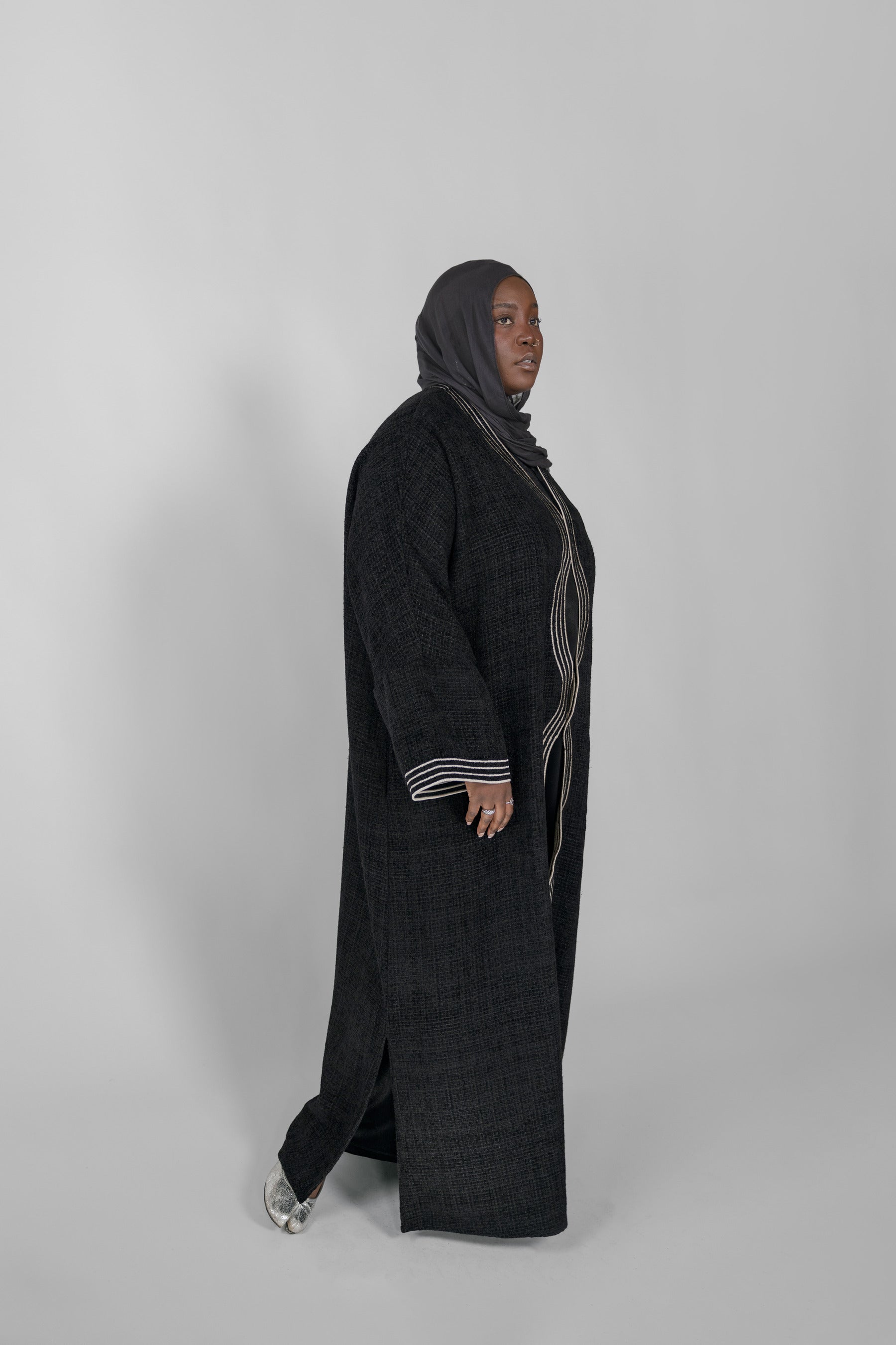 Person wearing a long black abaya with a hijab on a white background