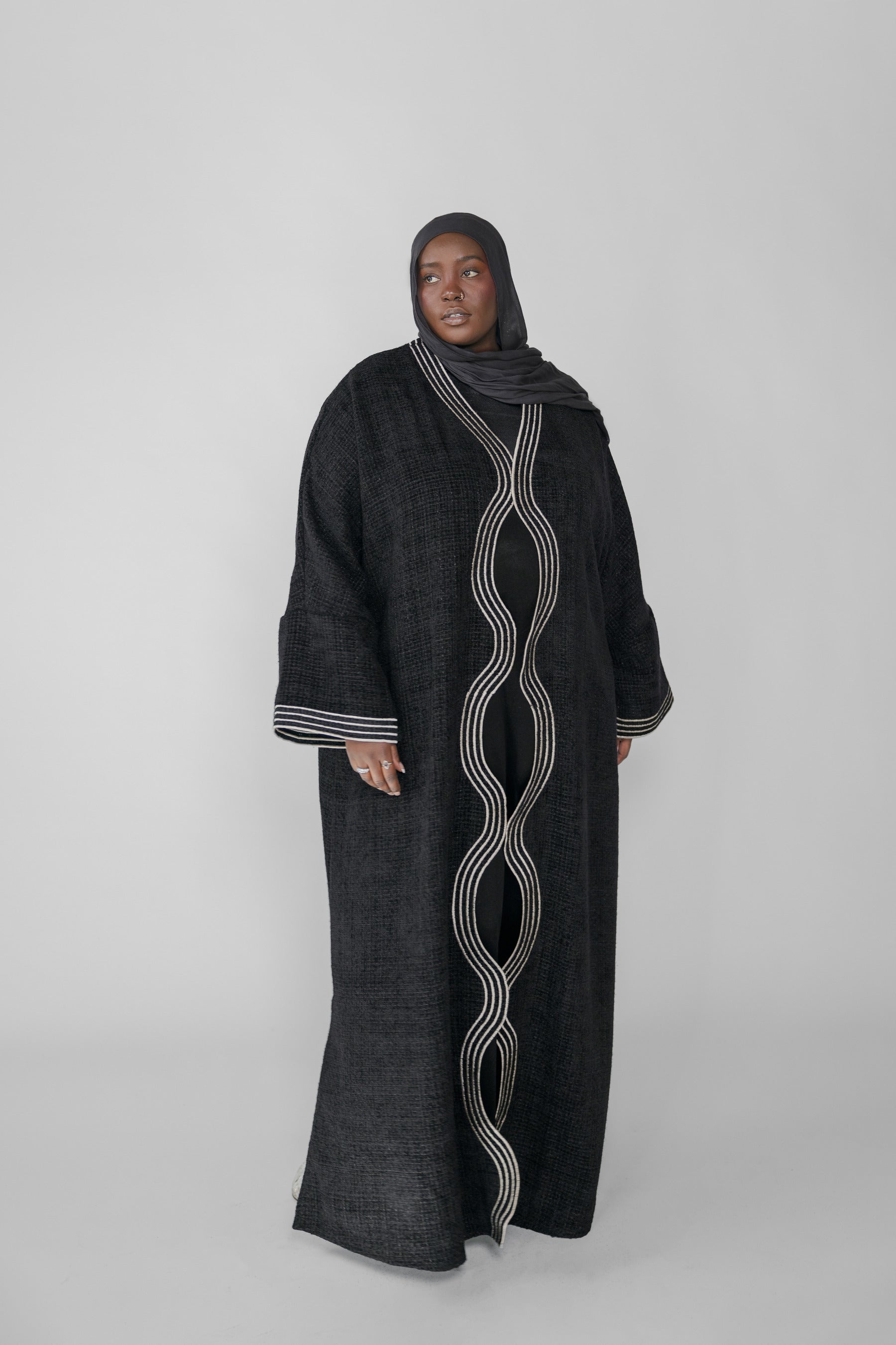 Woman wearing a black abaya with white embroidery on a white background
