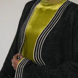Person wearing a black abaya with white trim over a green top against a neutral background