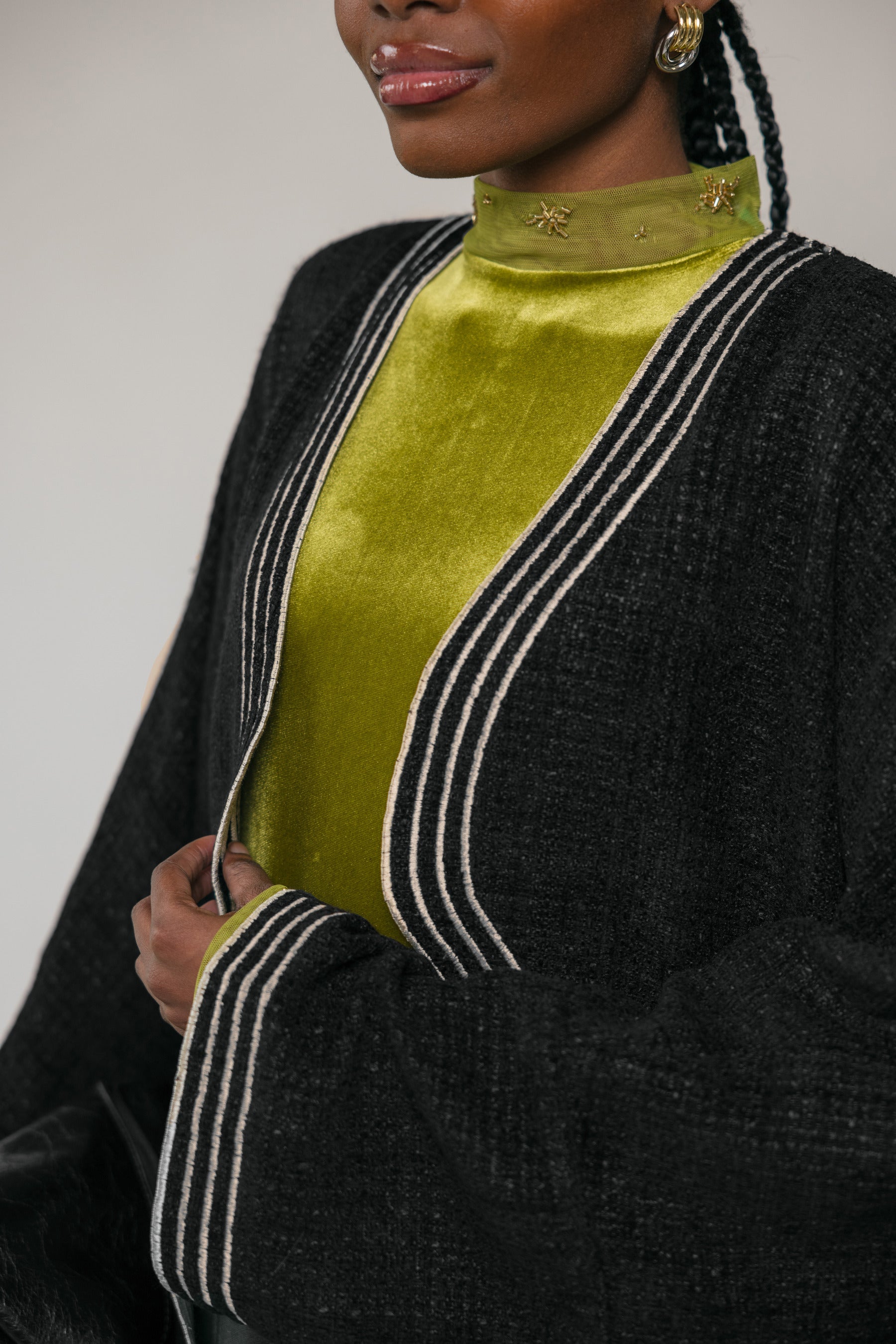 Person wearing a black abaya with white trim over a green top against a neutral background