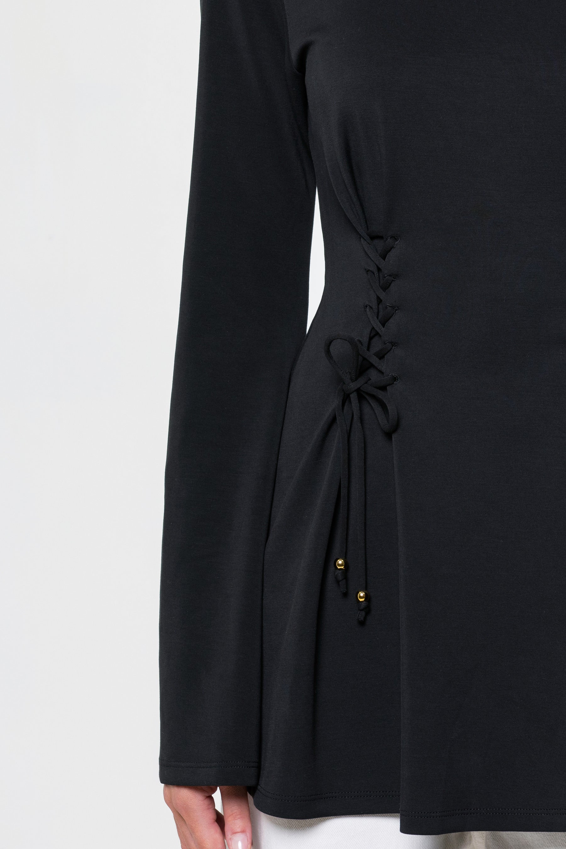 Close-up of a black long-sleeve dress with a lace-up side detail and small gold bead accents, shown on a model against a light gray background.