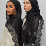 Two women wearing black sheer hijabs with black lace trim, posed against a light gray studio background.