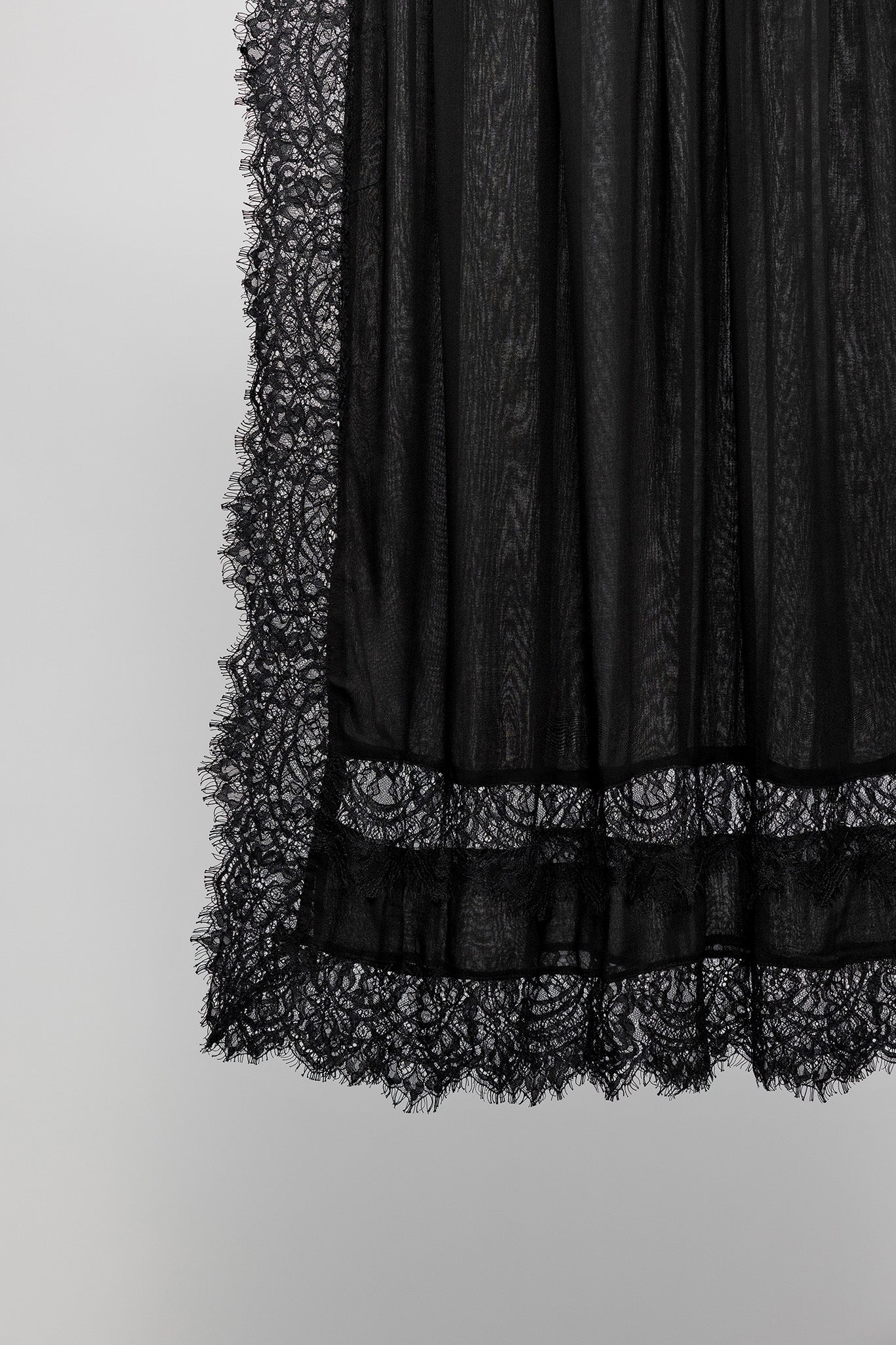 Black sheer lace skirt with a textured pattern and a wide lace hem, shown against a plain light gray background.