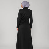 Person wearing a black dress and headscarf on a gray background