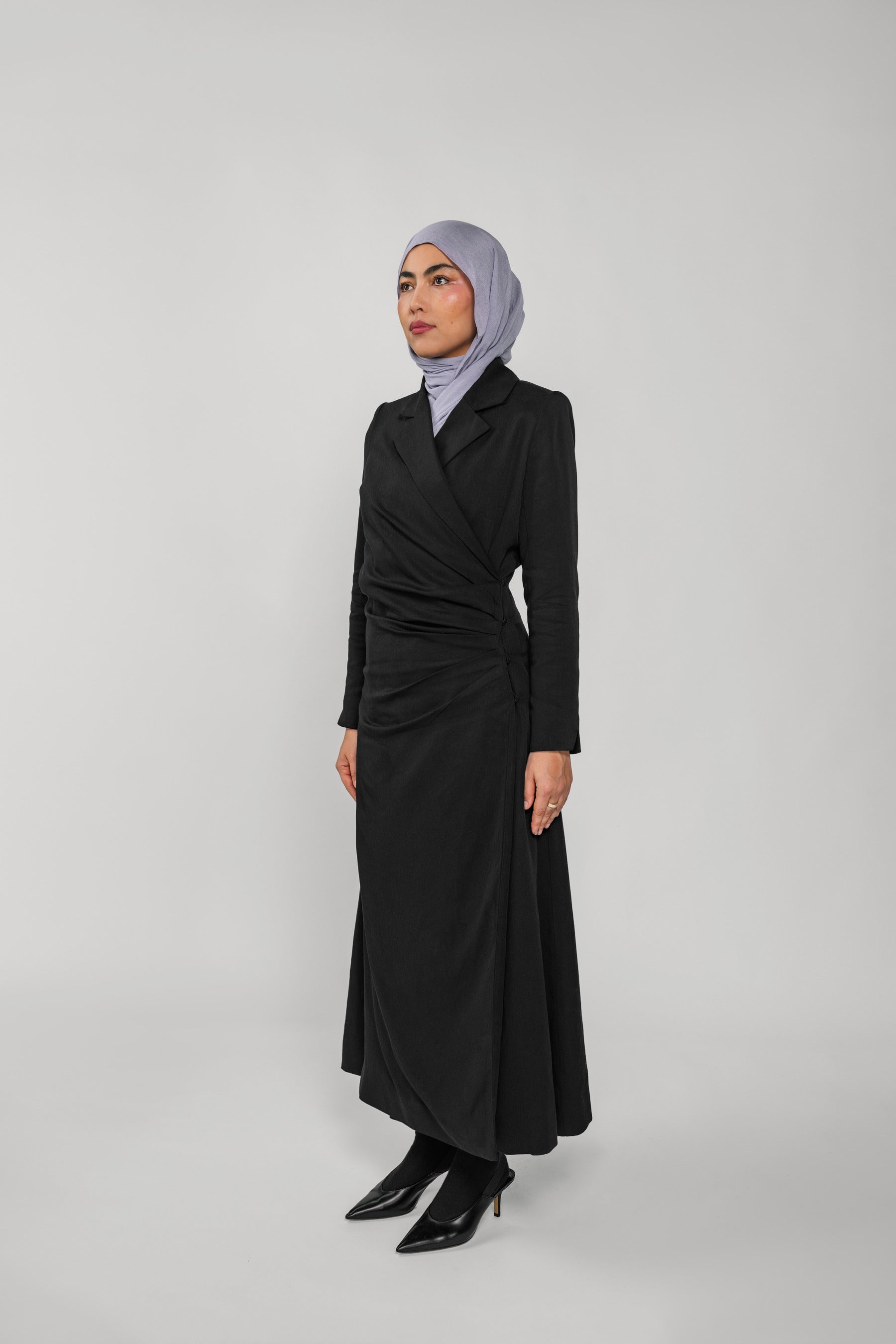 Woman wearing a black ruched abaya and gray hijab on a white background