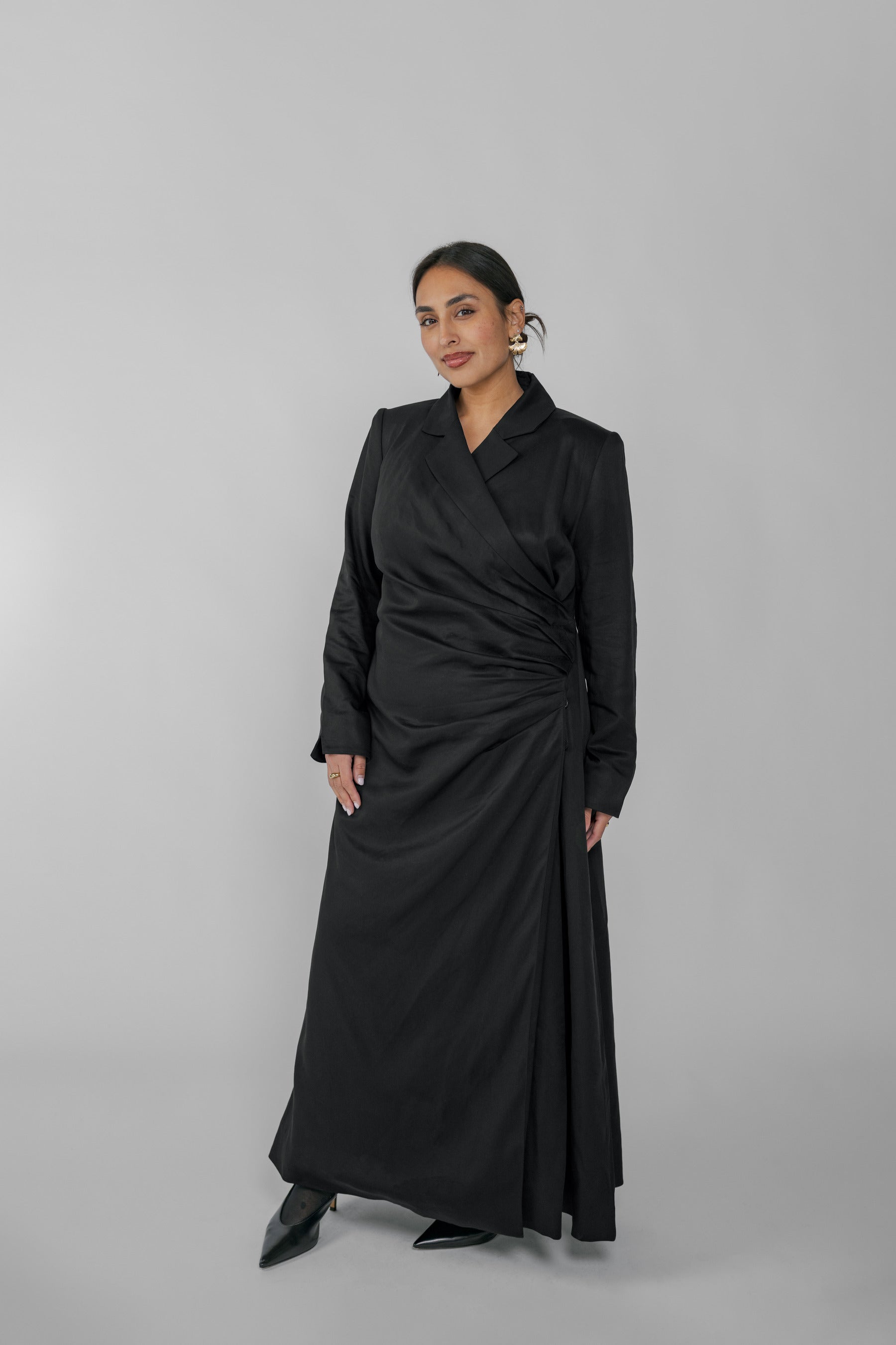 Woman wearing a black ruched dress against a gray background