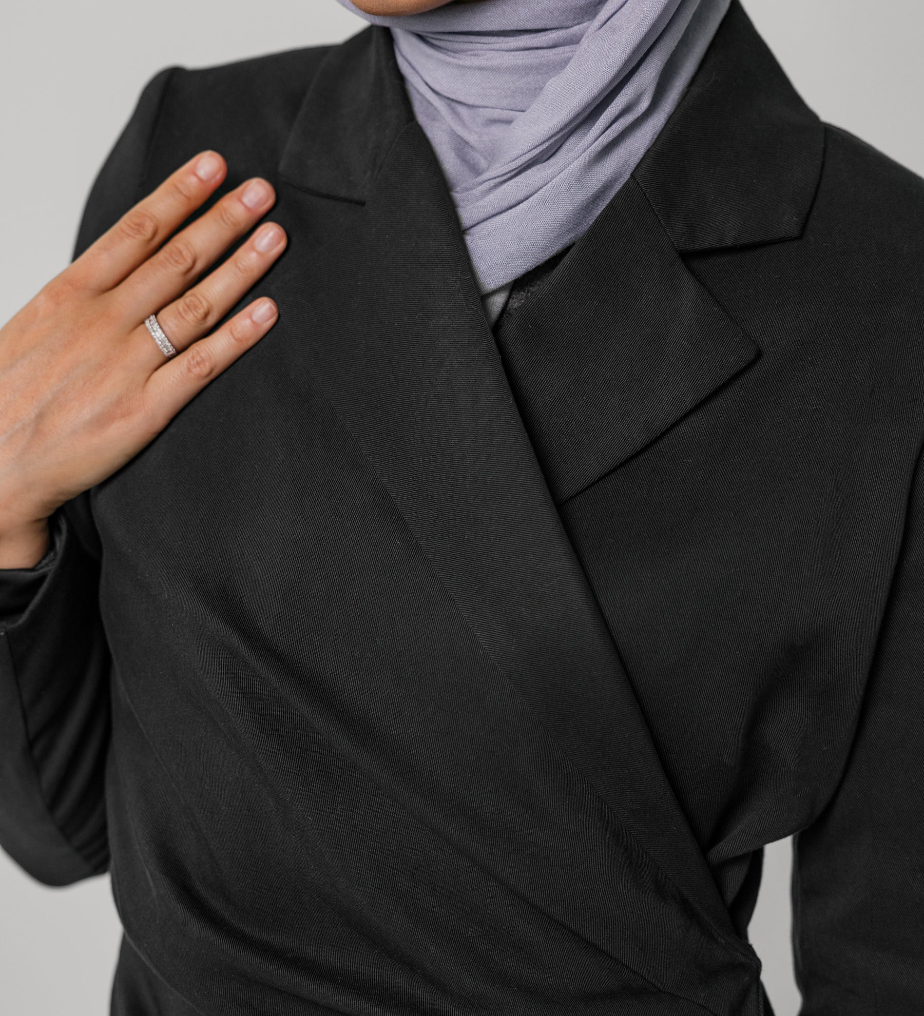Person wearing a black ruched abaya and light gray hijab on a plain background