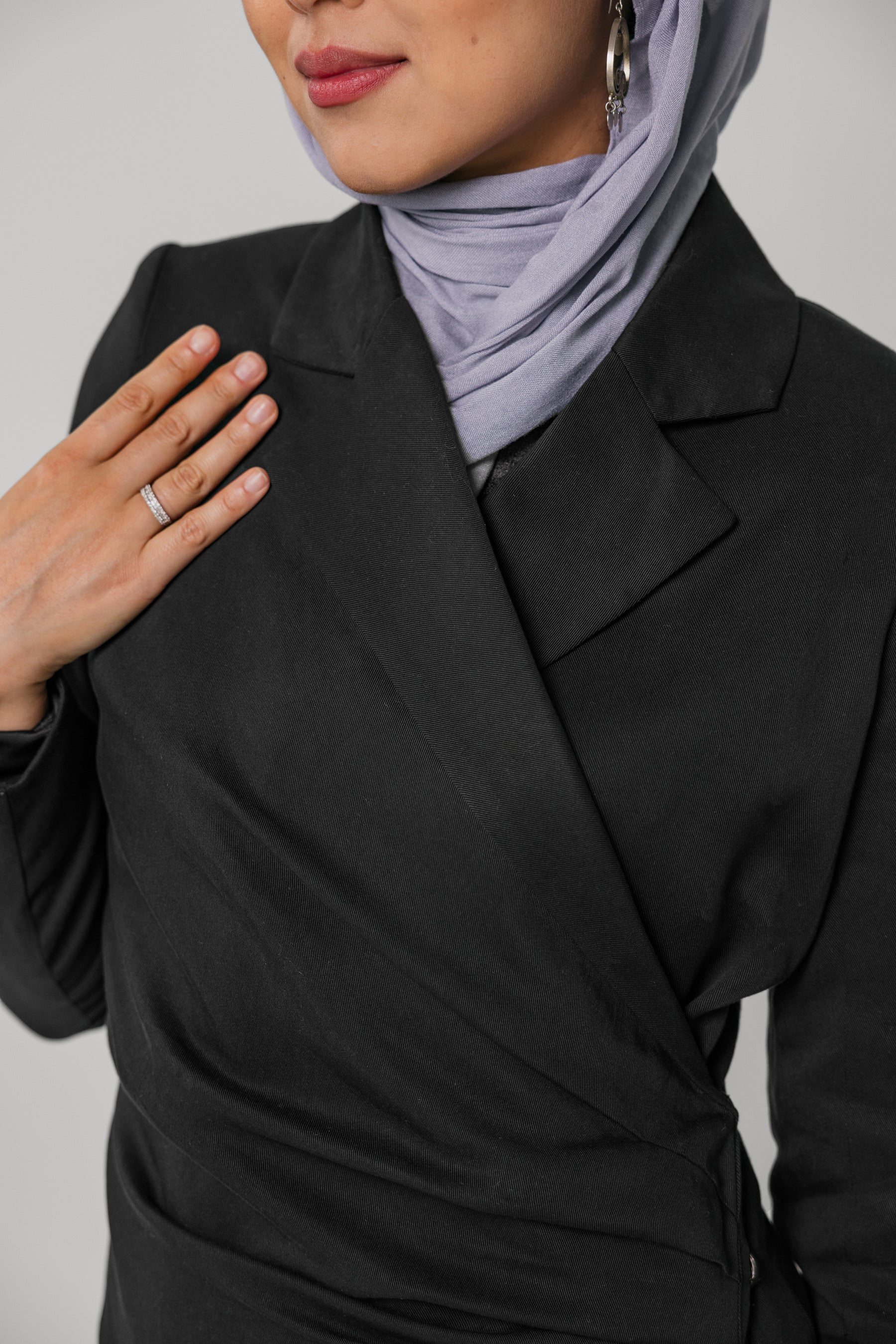 Person wearing a black ruched abaya and light gray hijab on a plain background