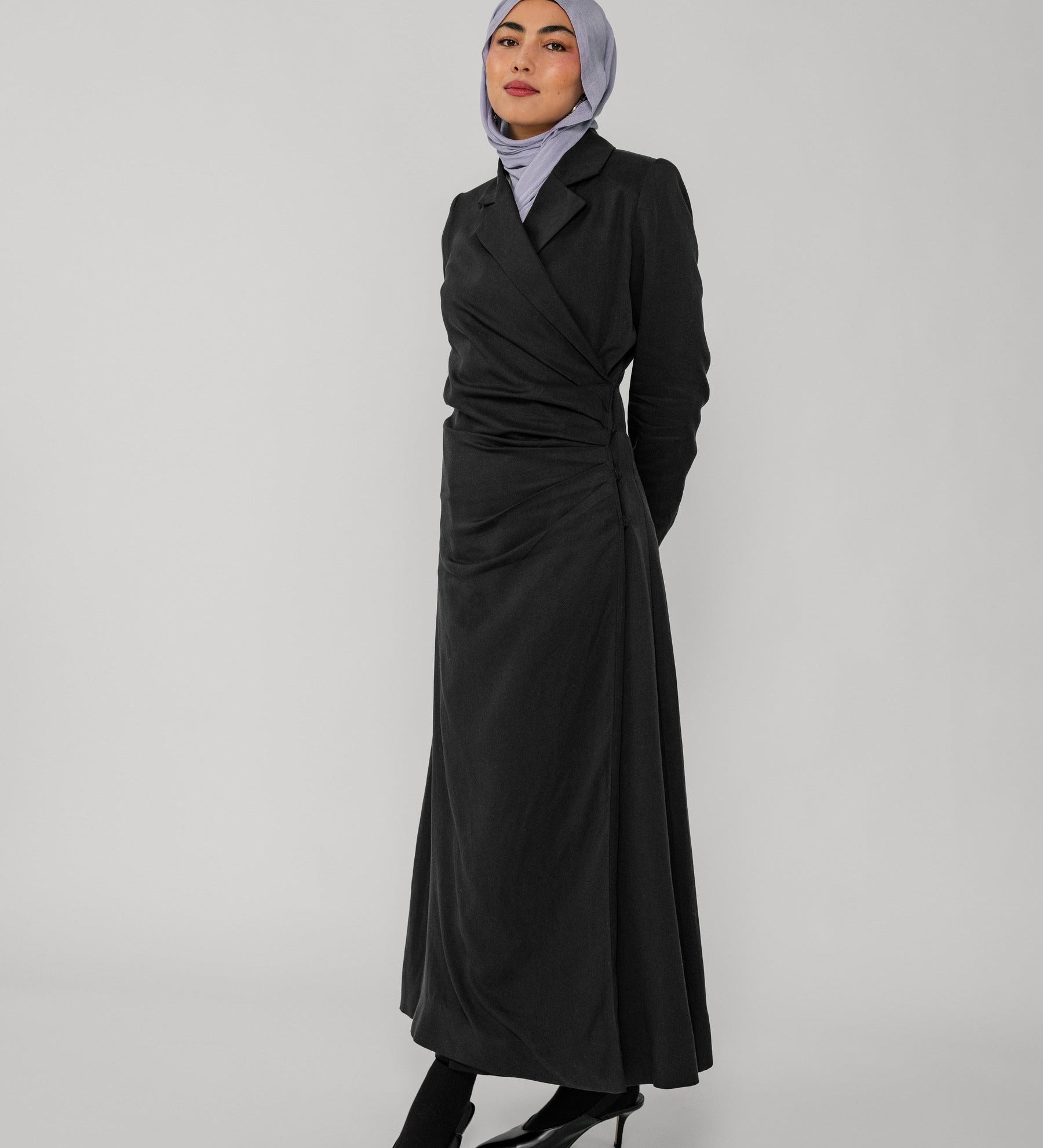 Woman wearing a black wrap abaya and gray hijab on a white background