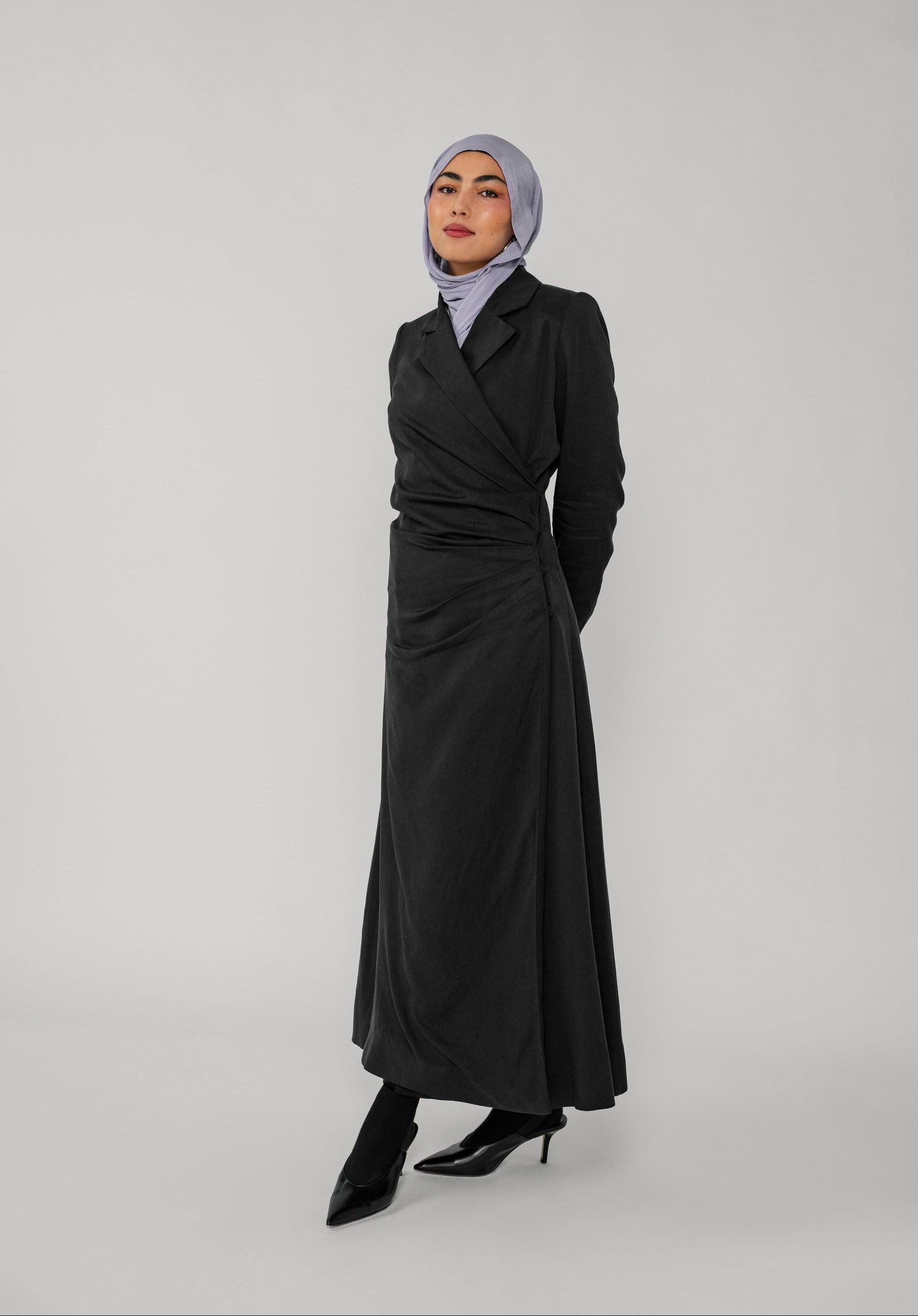 Woman wearing a black wrap abaya and gray hijab on a white background