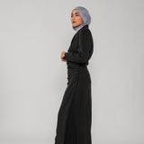 Woman wearing a black ruched abaya and gray hijab on a white background