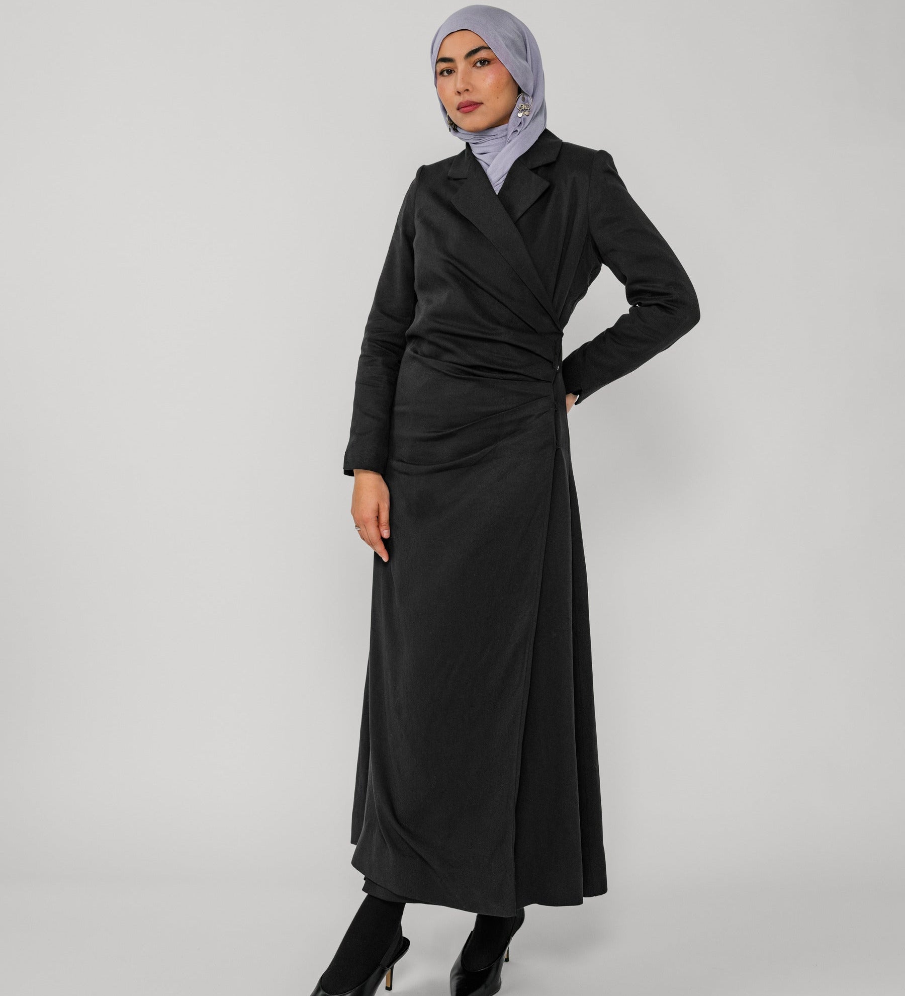 Woman wearing a black ruched abaya and gray hijab on a white background