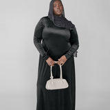 Woman wearing a black abaya with a hijab, holding a white handbag on a light gray background