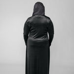 Person wearing a black abaya with a hijab on a light gray background