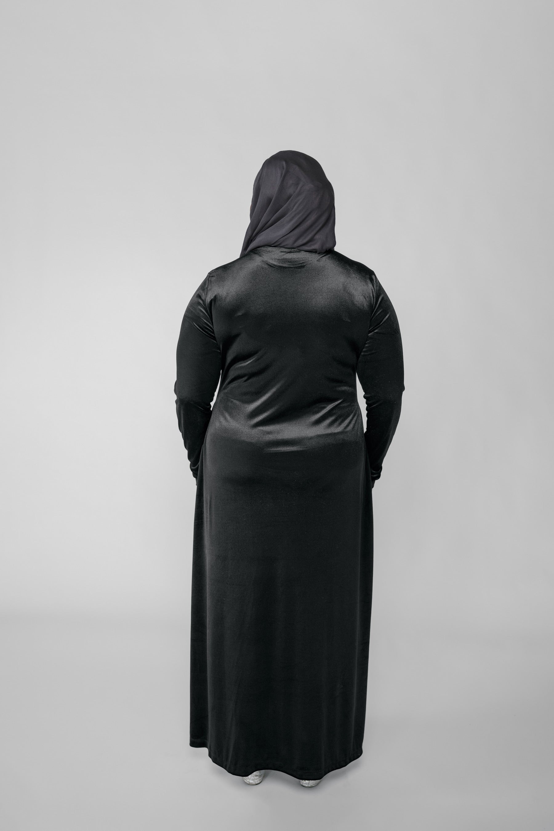 Person wearing a black abaya with a hijab on a light gray background
