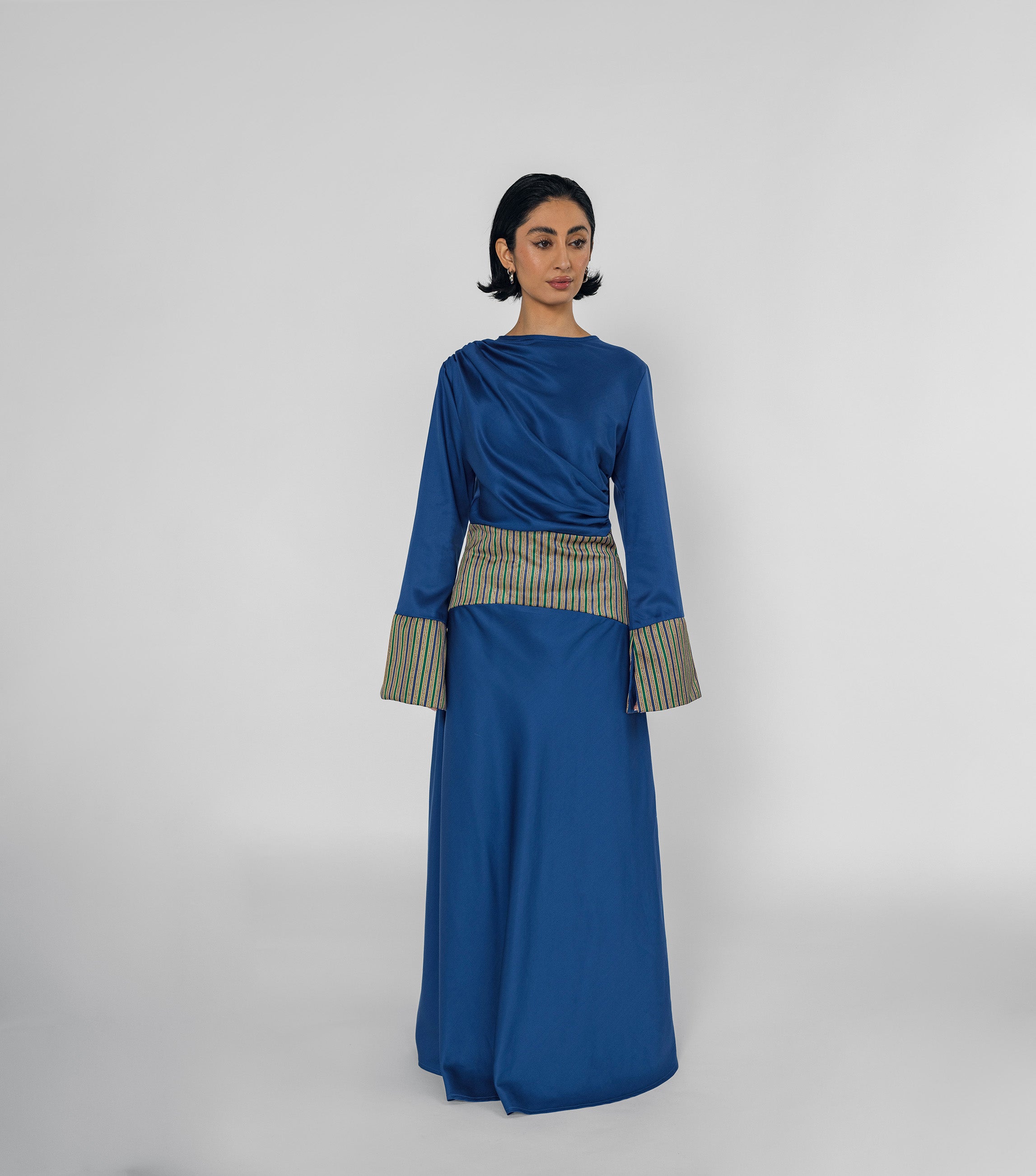 Woman wearing a blue dress with a patterned belt on a white background