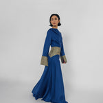 Woman wearing a blue dress with patterned cuffs on a white background