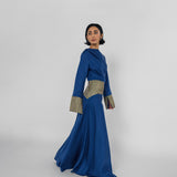 Woman wearing a blue dress with patterned cuffs on a white background