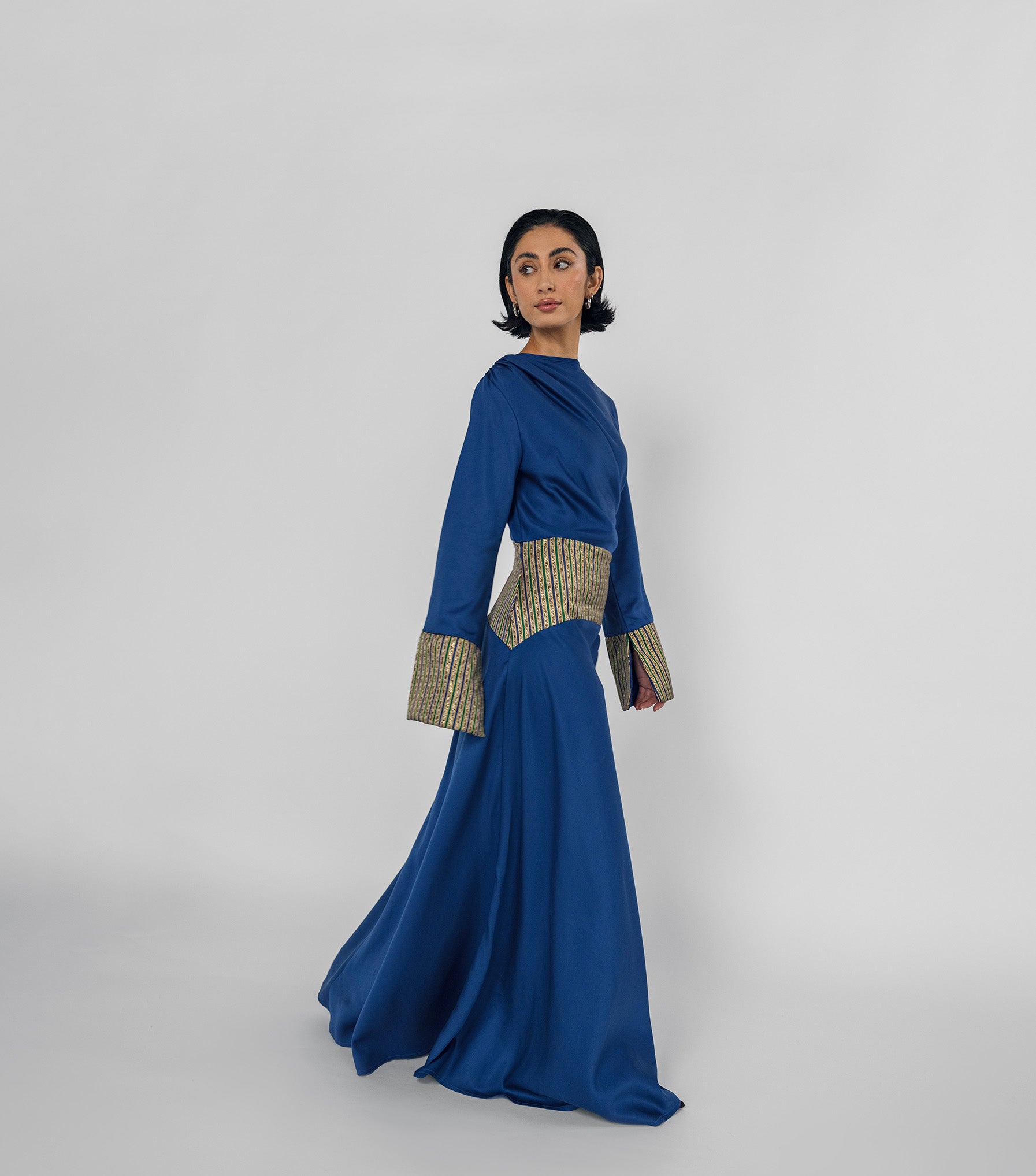 Woman wearing a blue dress with patterned cuffs on a white background