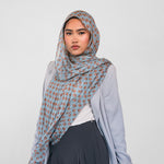Woman wearing a light blue patterned hijab, light blue cardigan, white top, and dark pants on a white background
