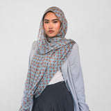 Woman wearing a light blue patterned hijab, light blue cardigan, white top, and dark pants on a white background