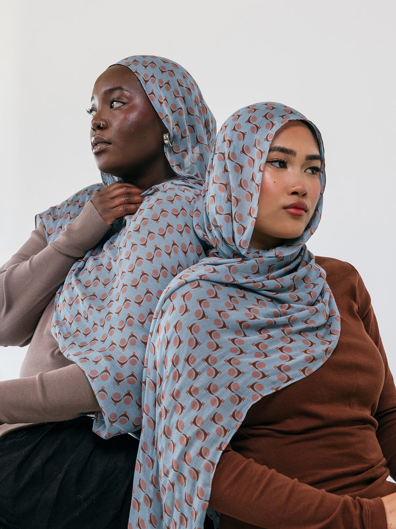 Two women wearing patterned hijabs against a white background