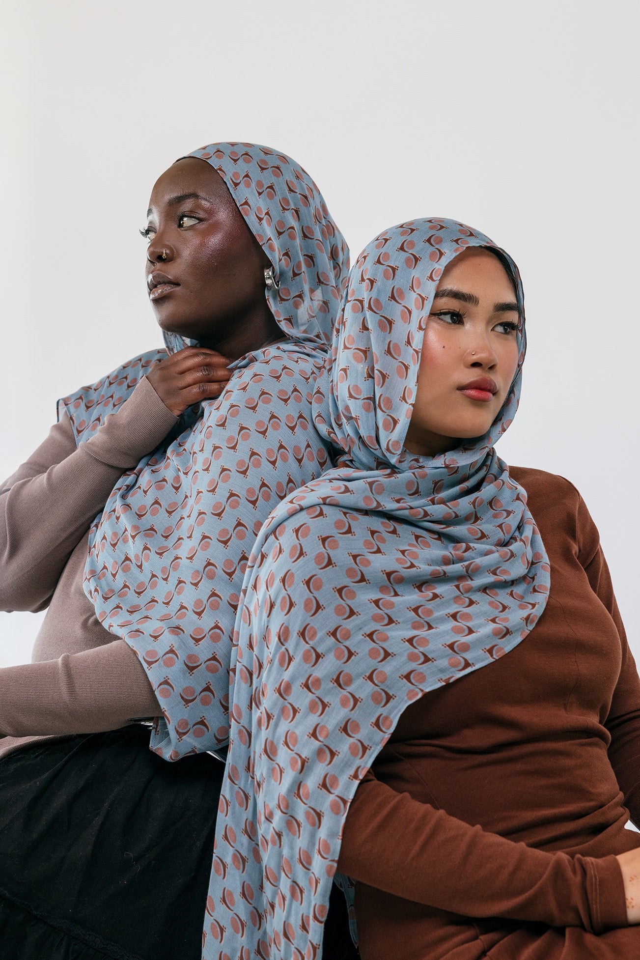 Two women wearing patterned hijabs against a white background