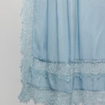 A close-up of a light blue sheer fabric with layered ruffles and delicate lace trim along the bottom edge, shown against a plain light gray background.
