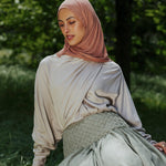 Woman in a hijab sitting on a tree stump in a natural setting