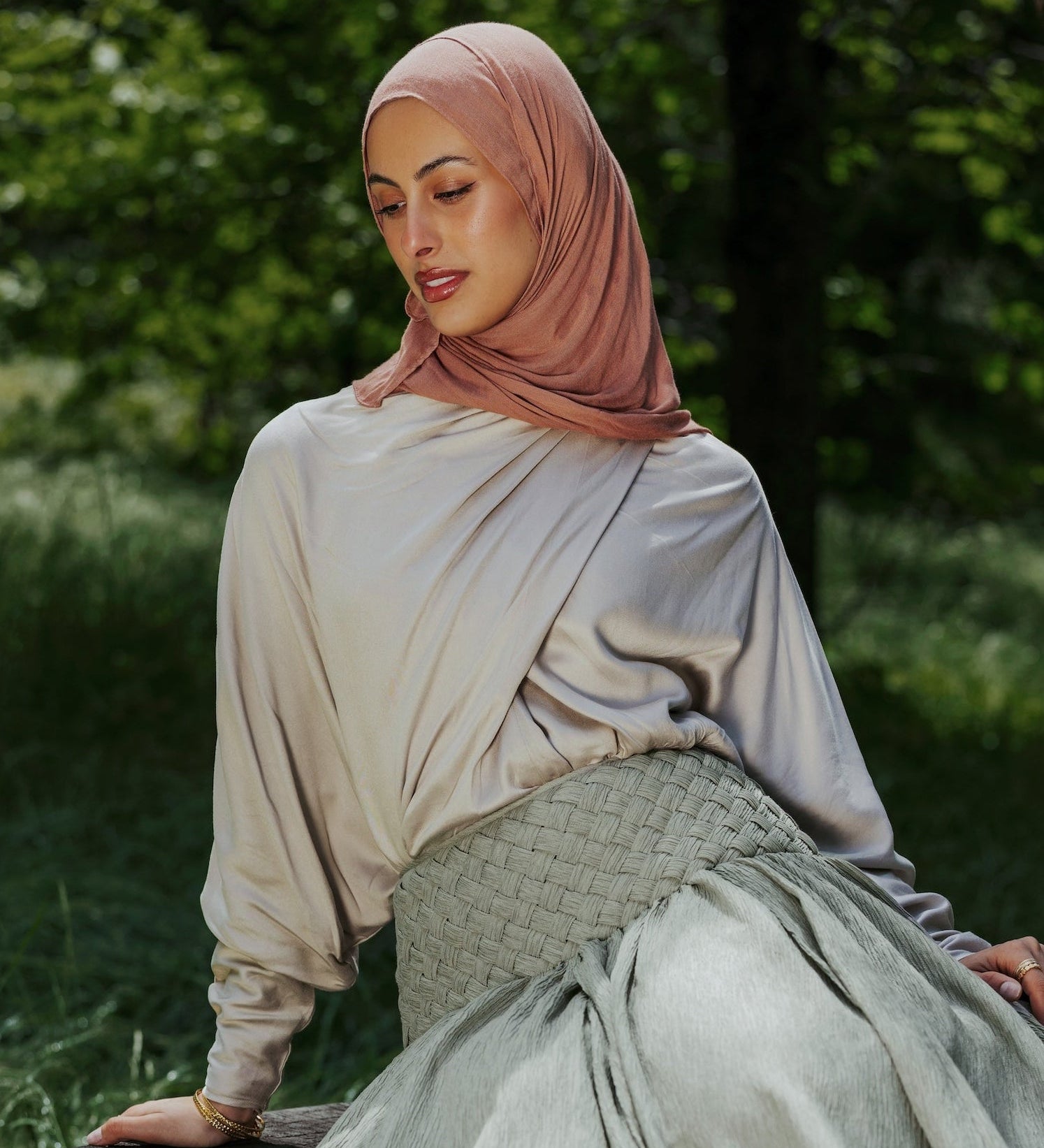 Woman in a hijab sitting on a tree stump in a natural setting