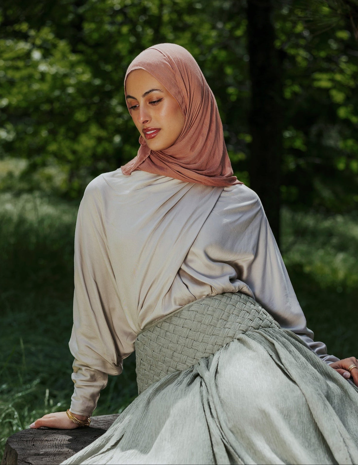 Woman in a hijab sitting on a tree stump in a natural setting