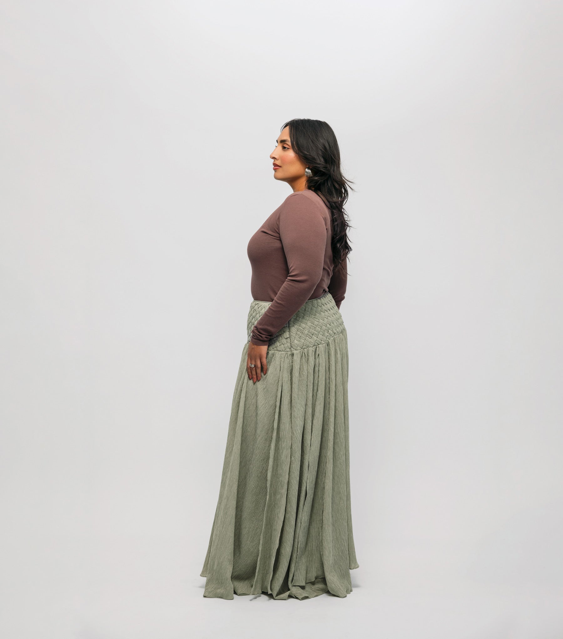Woman wearing a brown-colored top, and green skirt on a white background