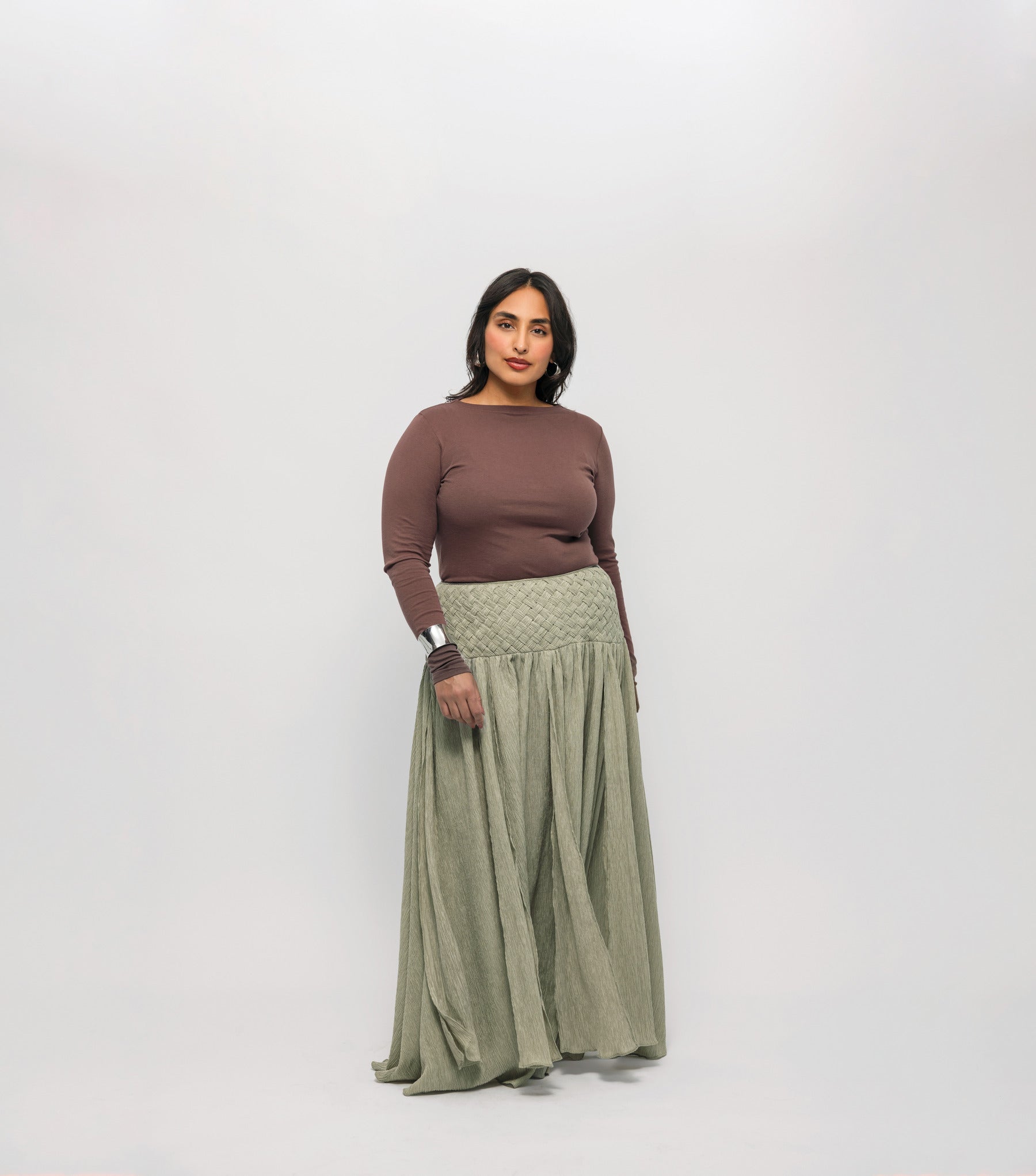 Woman wearing a brown-colored top, and green skirt on a white background