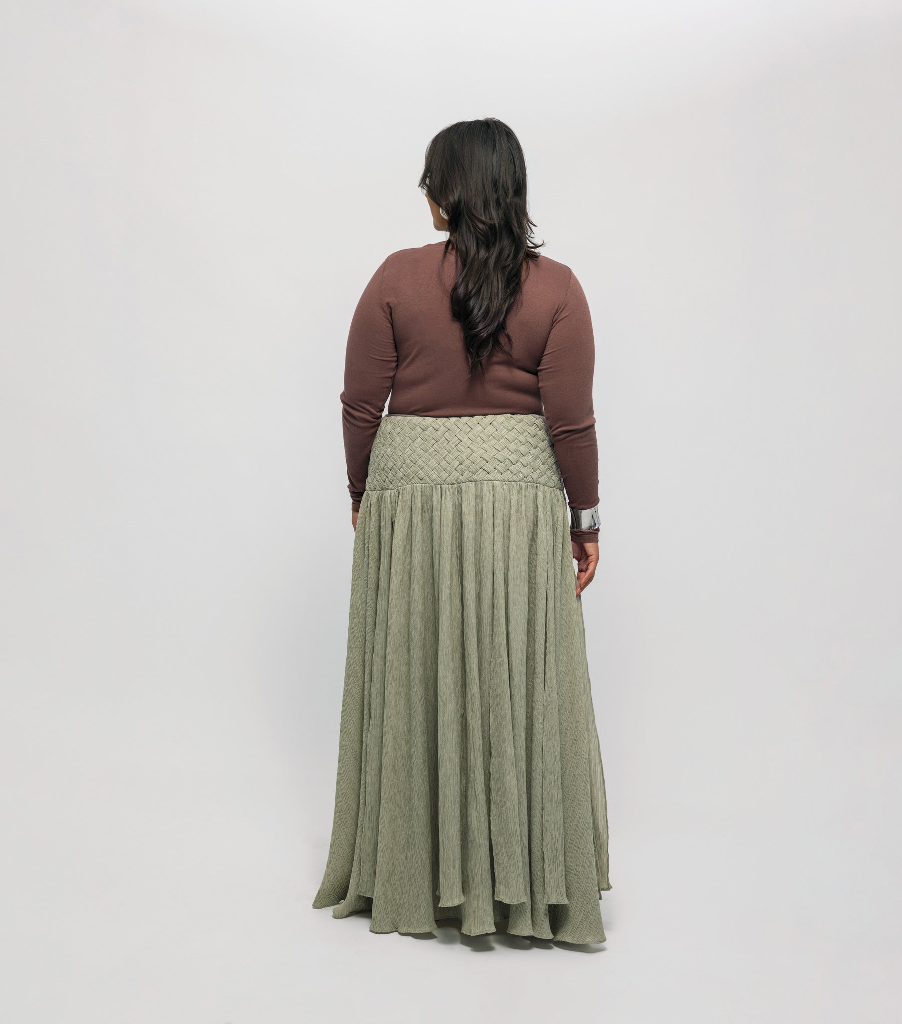 Woman wearing a brown-colored top, and green skirt on a white background