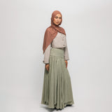 Woman wearing a hijab, light-colored top, and green skirt on a white background