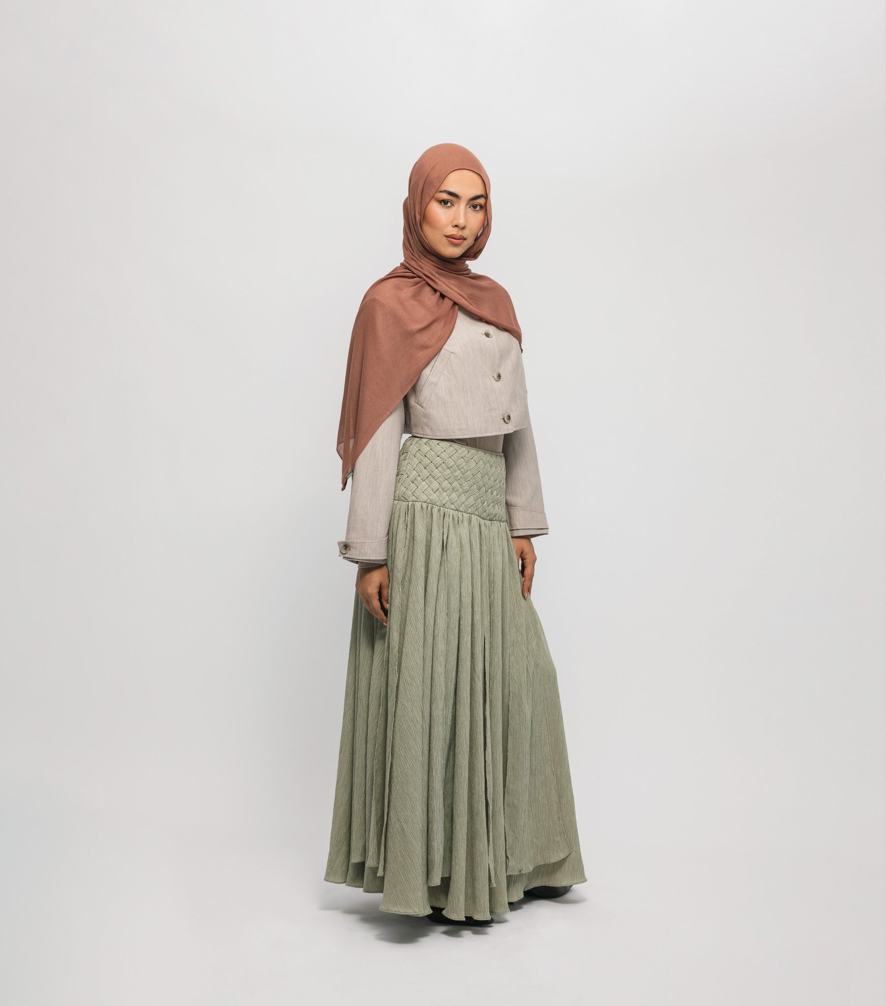 Woman wearing a hijab, light-colored top, and green skirt on a white background