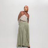 Woman wearing a hijab, light-colored top, and green skirt on a white background