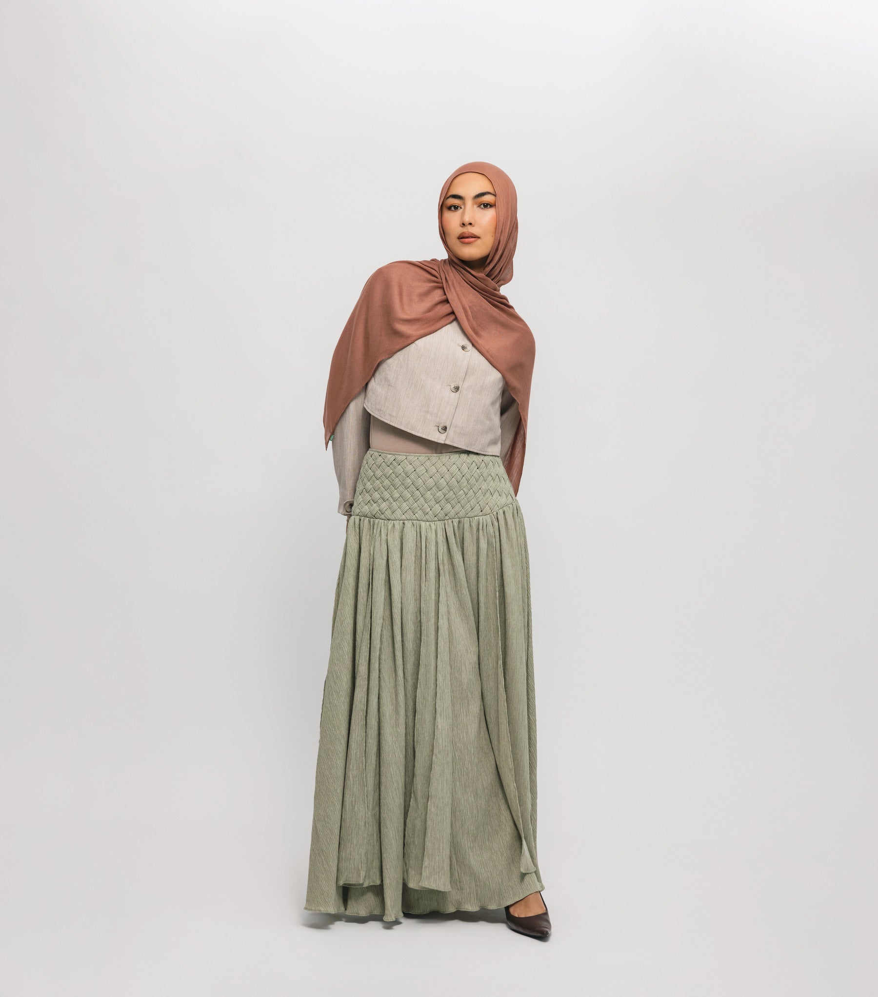 Woman wearing a hijab, light-colored top, and green skirt on a white background