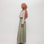 Woman wearing a hijab, light-colored top, and green skirt on a white background