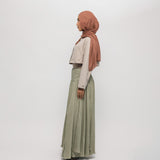 Woman wearing a hijab, light-colored top, and green skirt on a white background