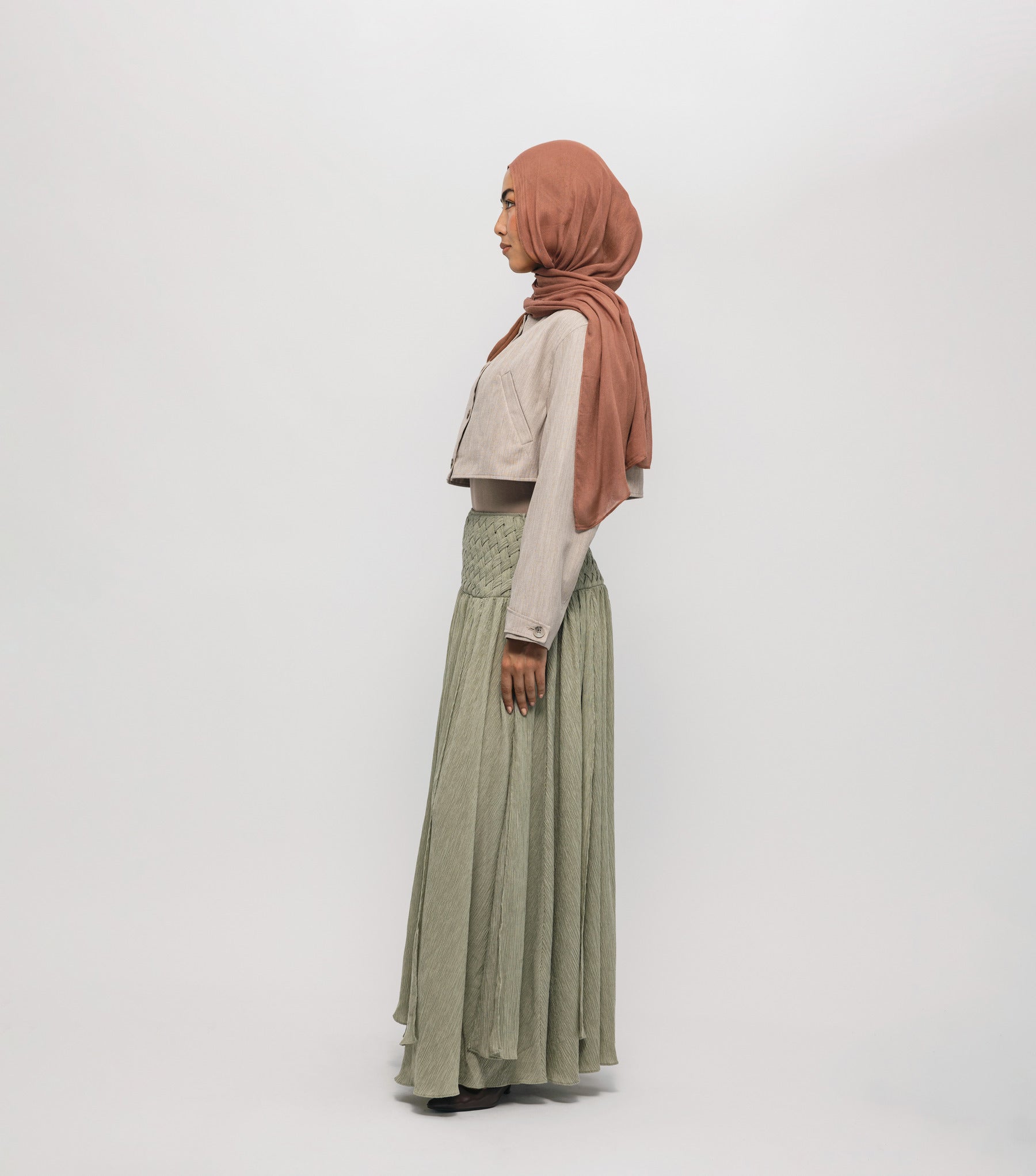 Woman wearing a hijab, light-colored top, and green skirt on a white background